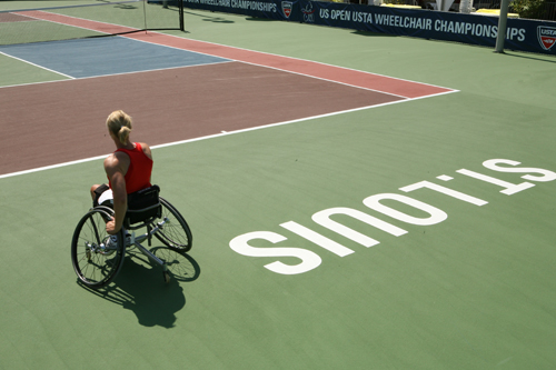 A woman in a wheelchair waits on a tennis court