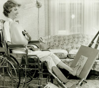 A young woman who uses a wheelchair paints on a canvas by holding the paintbrush with her toes.